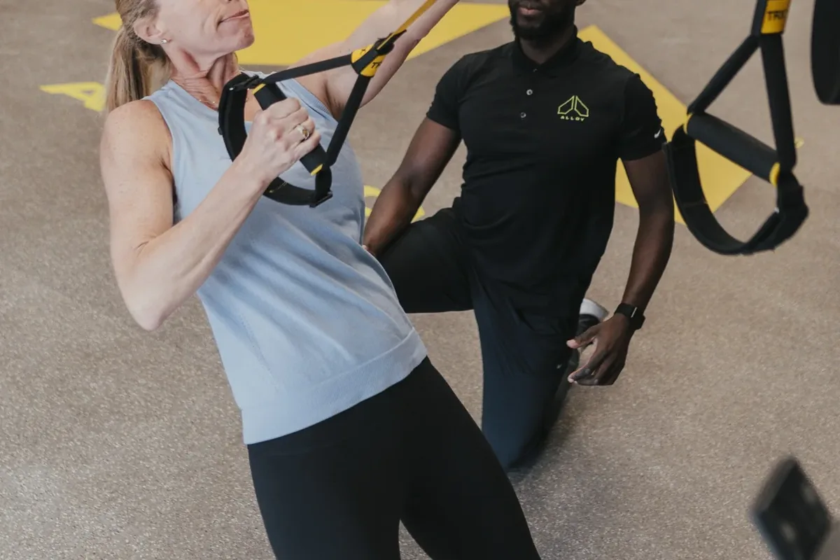 A kneeling coach guides a new member through a TRX pull exercise at Alloy Personal Training Middleton in Middleton, WI.