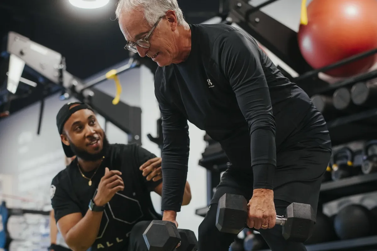 A coach encourages an older member mid dumbbell row during a coached session at Alloy Personal Training Middleton in Middleton, WI.