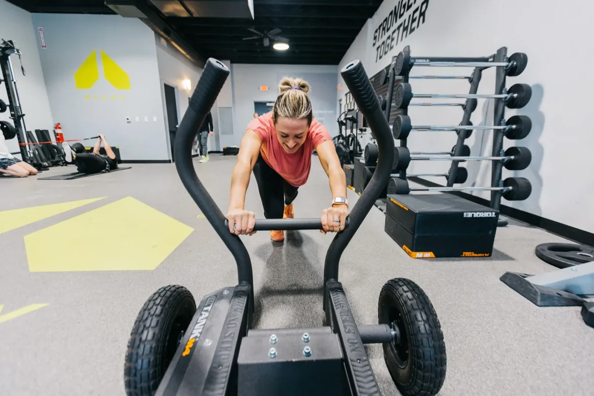 A member drives a weighted training sled across the turf at an Alloy Personal Training studio