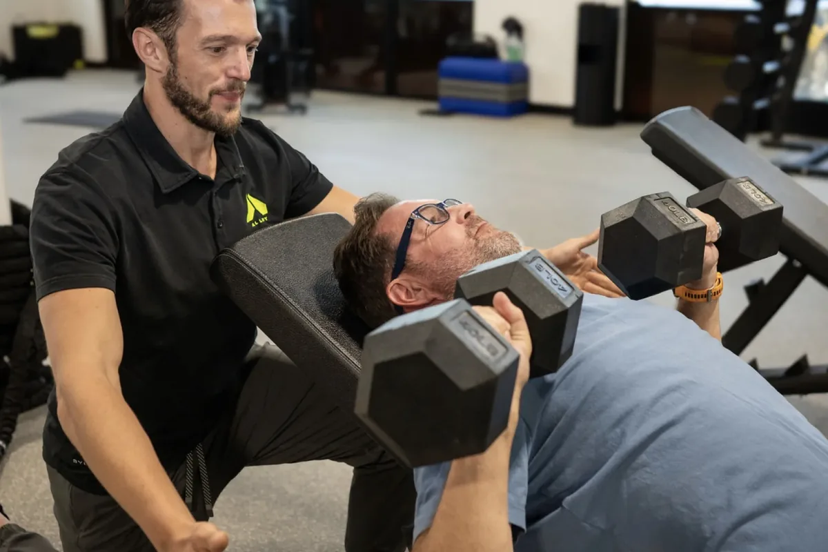 A coach guides a member through an incline dumbbell press at an Alloy Personal Training studio