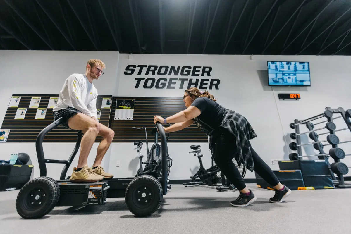 Two members work a weighted training sled together during a small group session