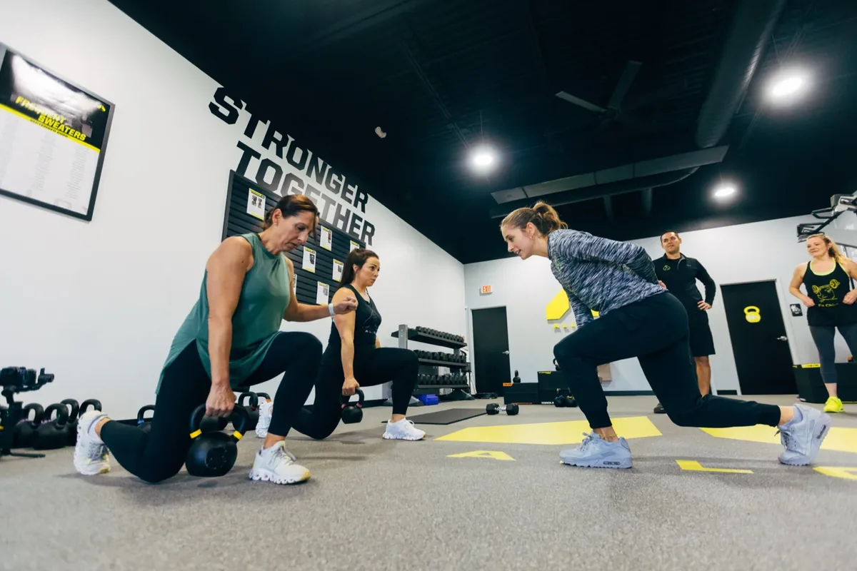 Members hold kettlebells in a split-stance lunge during a small group session at an Alloy Personal Training studio