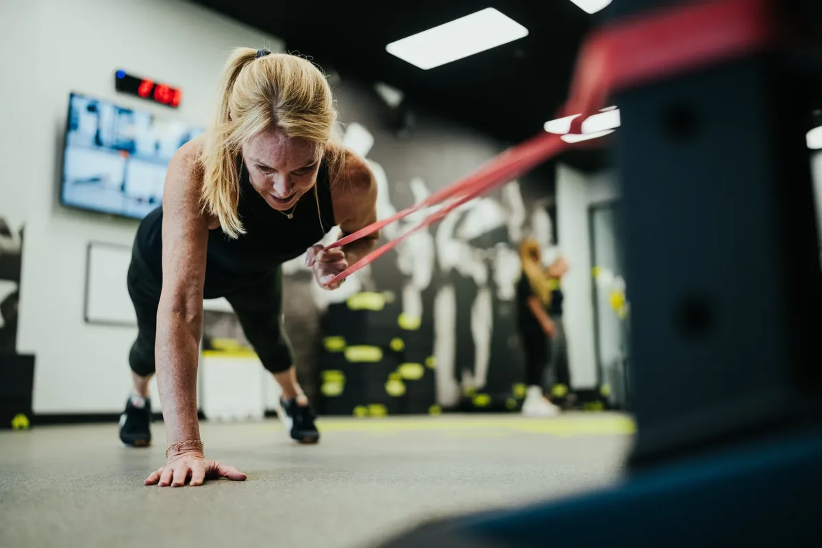 A woman holds a plank while pulling a resistance band during a strength session at an Alloy Personal Training studio